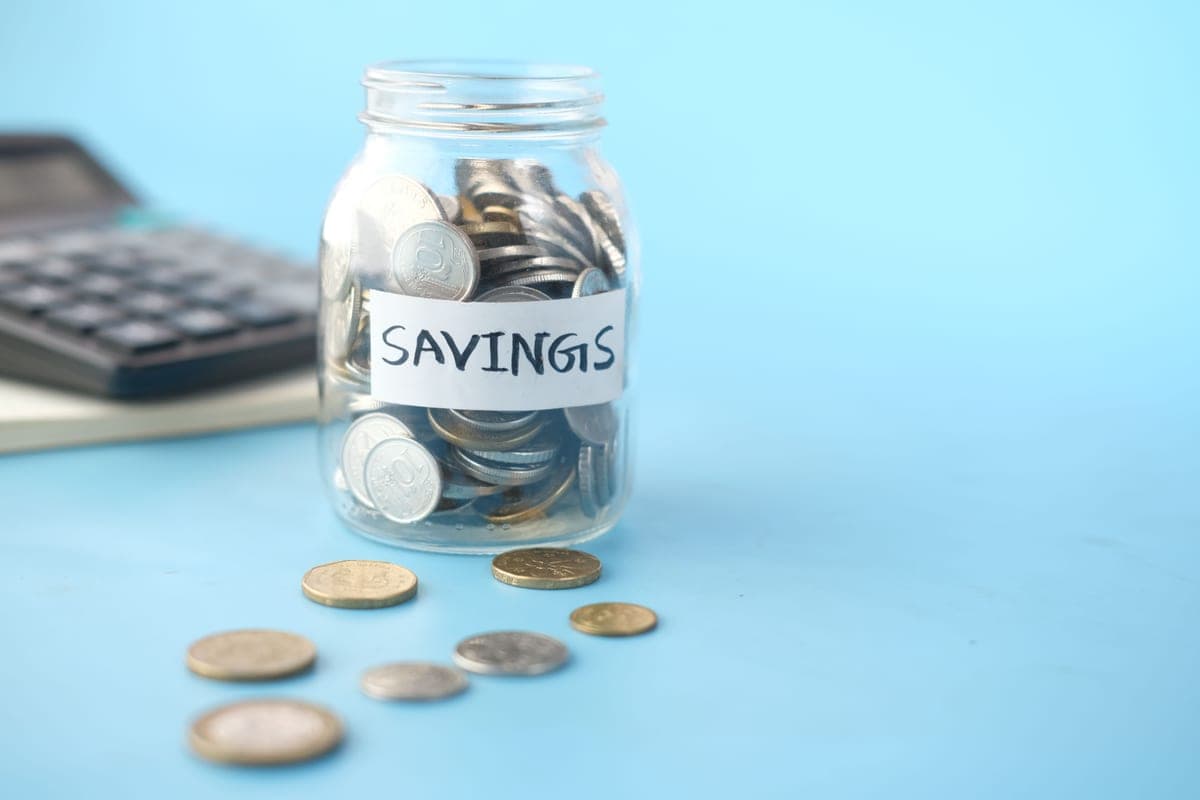 A glass jar labeled Savings filled with coins beside a calculator