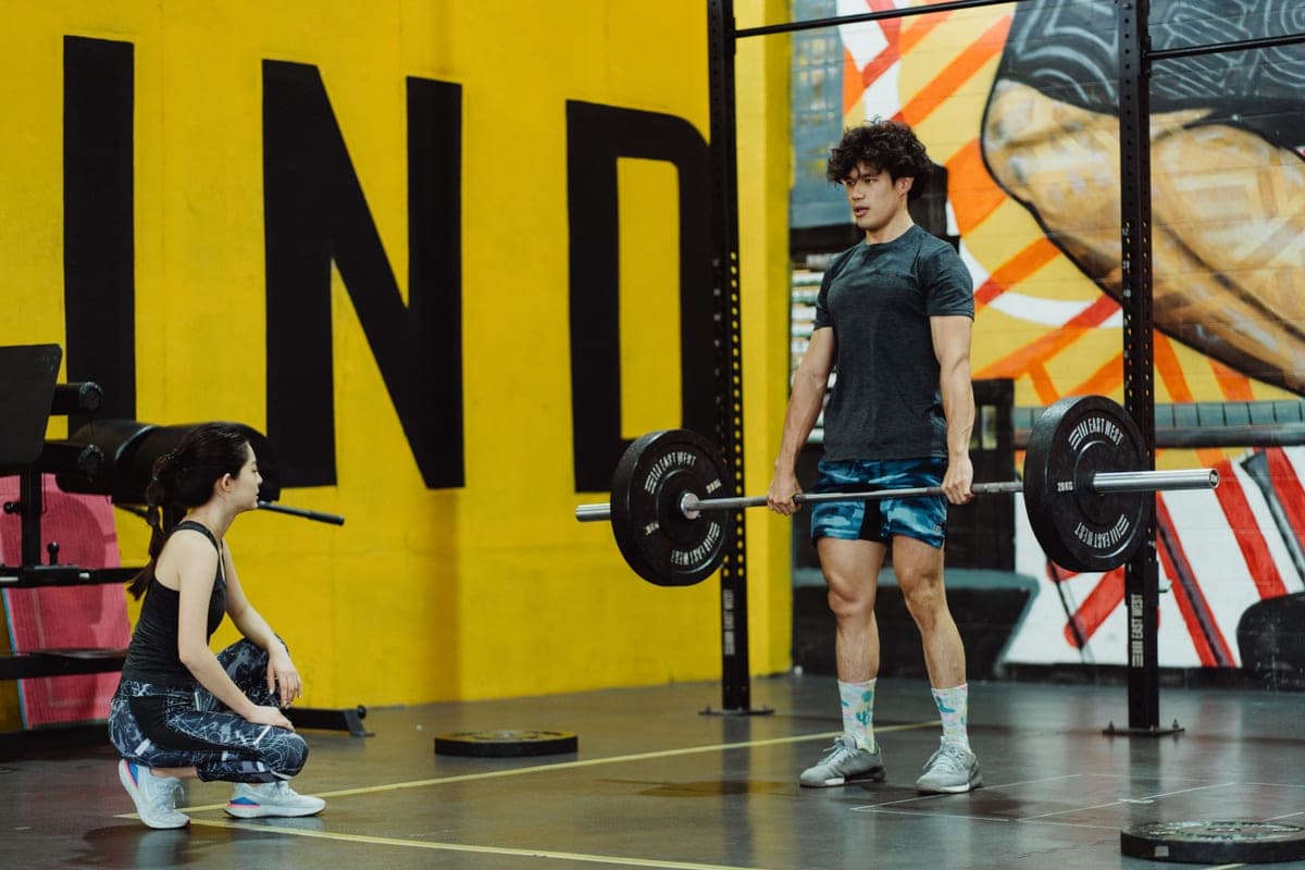 A man performing a deadlift in a gym while a trainer watches
