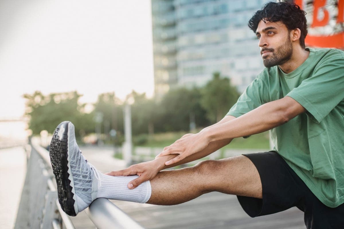 A man in a green shirt stretching his leg outdoors