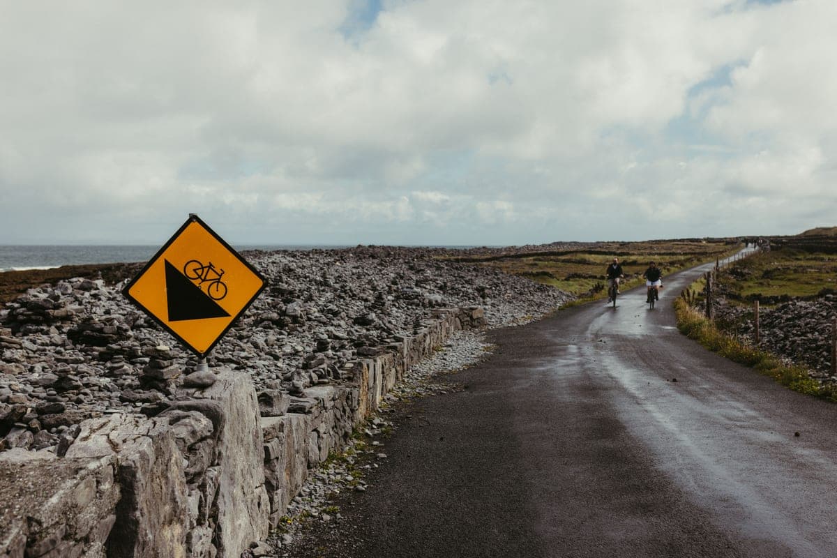 Two cyclists on a coastal road bordered by stone walls
