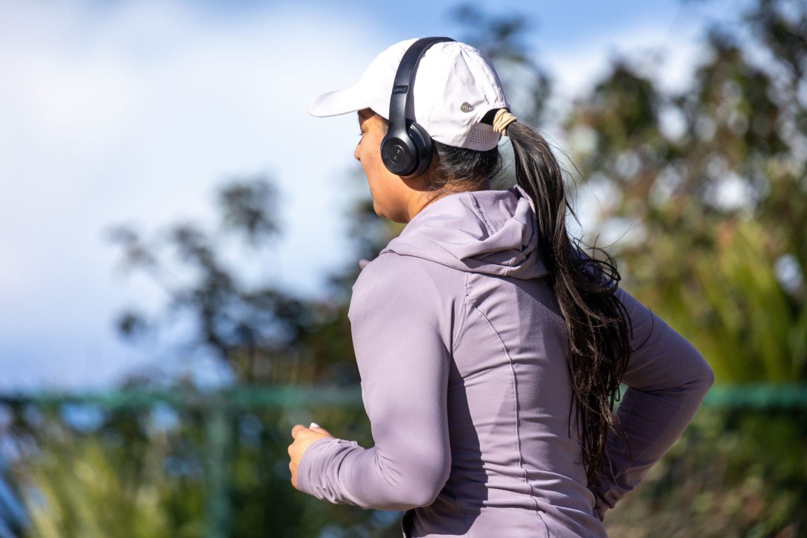 A woman jogging outdoors wearing headphones and a cap