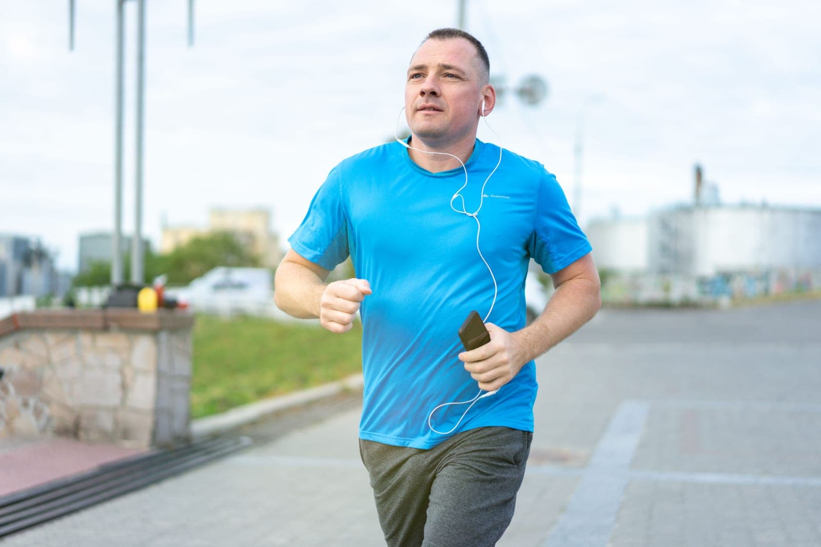 A man in a blue shirt jogging outdoors and listening to music on earphones